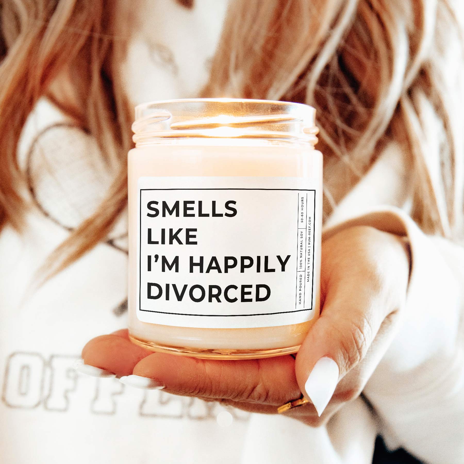 Smells Like I'm Happily Divorced 9oz Candle. The text is printed with big bold words. Held by a model.